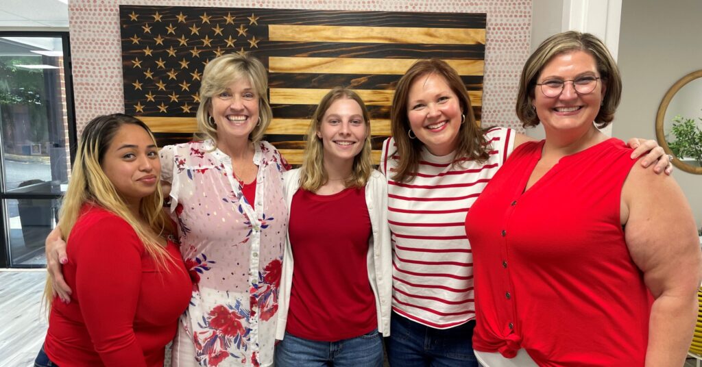 Intern smiling and posing with co-workers, all gathered together and looking cheerful in a group photo at the workplace.